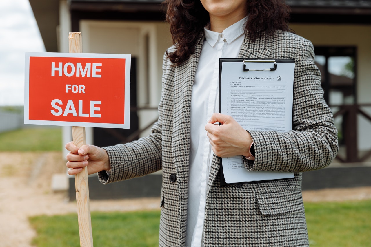 a woman holding a home for sale sign